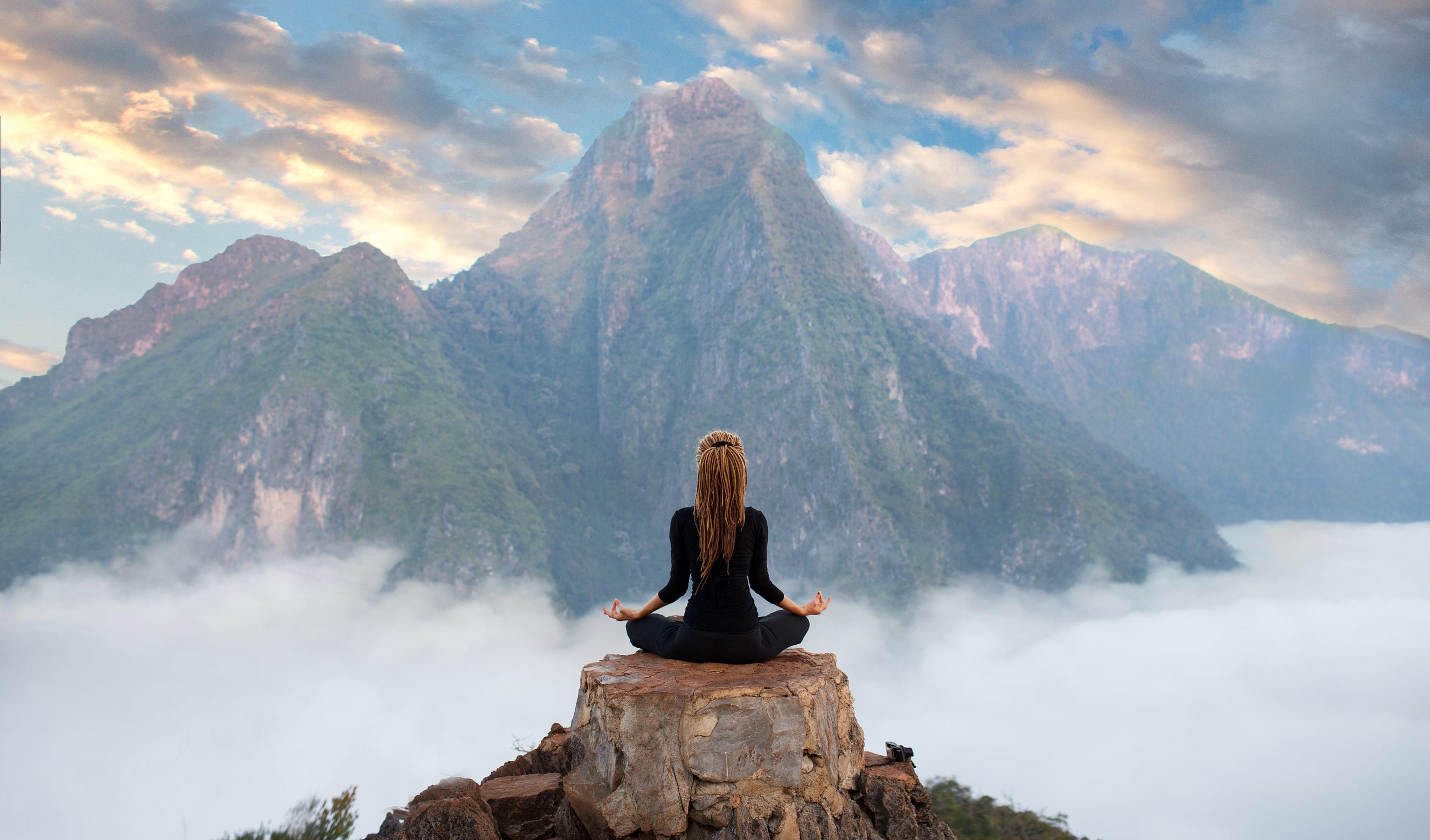 Woman meditating at the peak of mountain with other mountains around her.