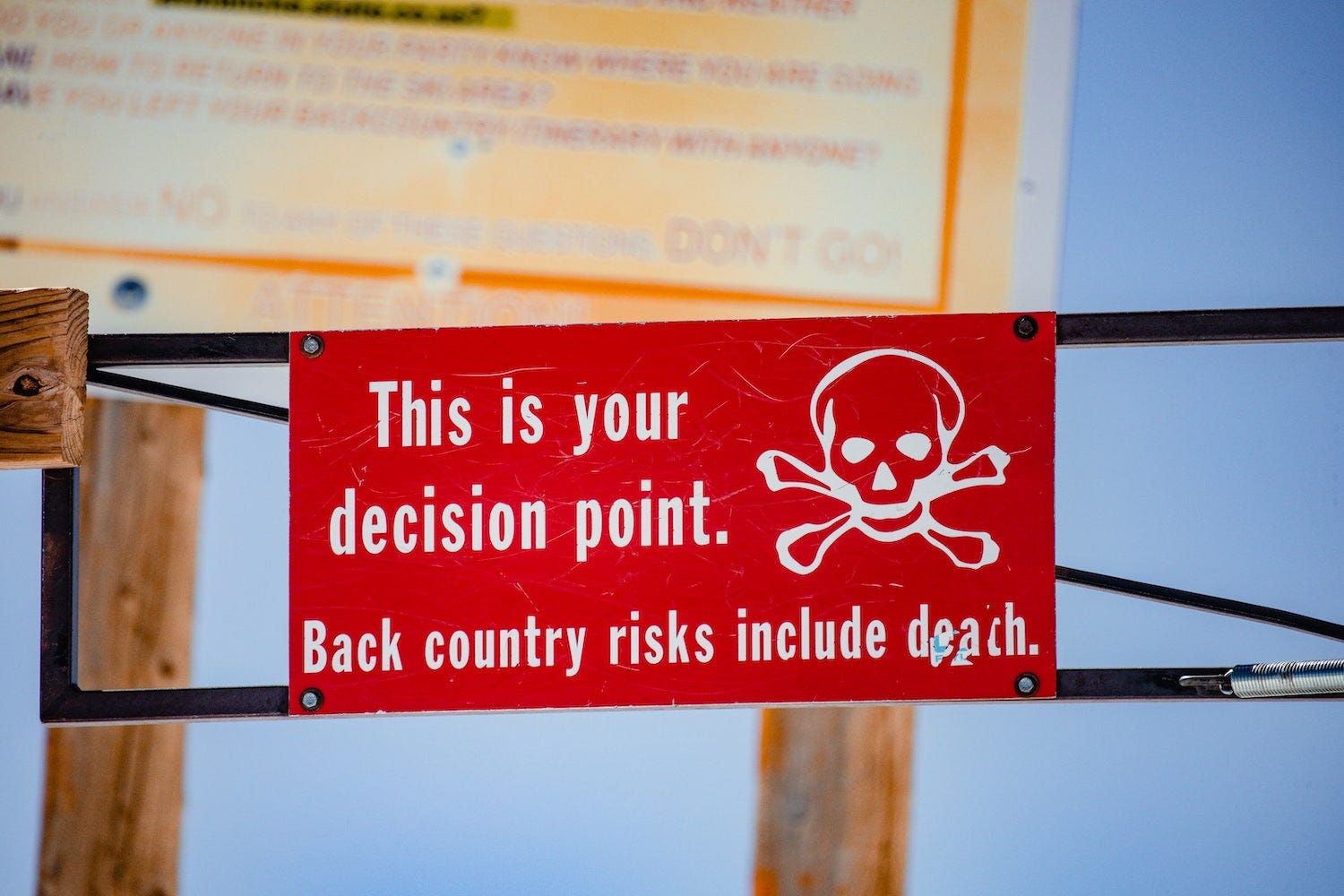 red sign with skull and cross bones reading "This is your decision point back country risks include death" showing severity of making some decisions
