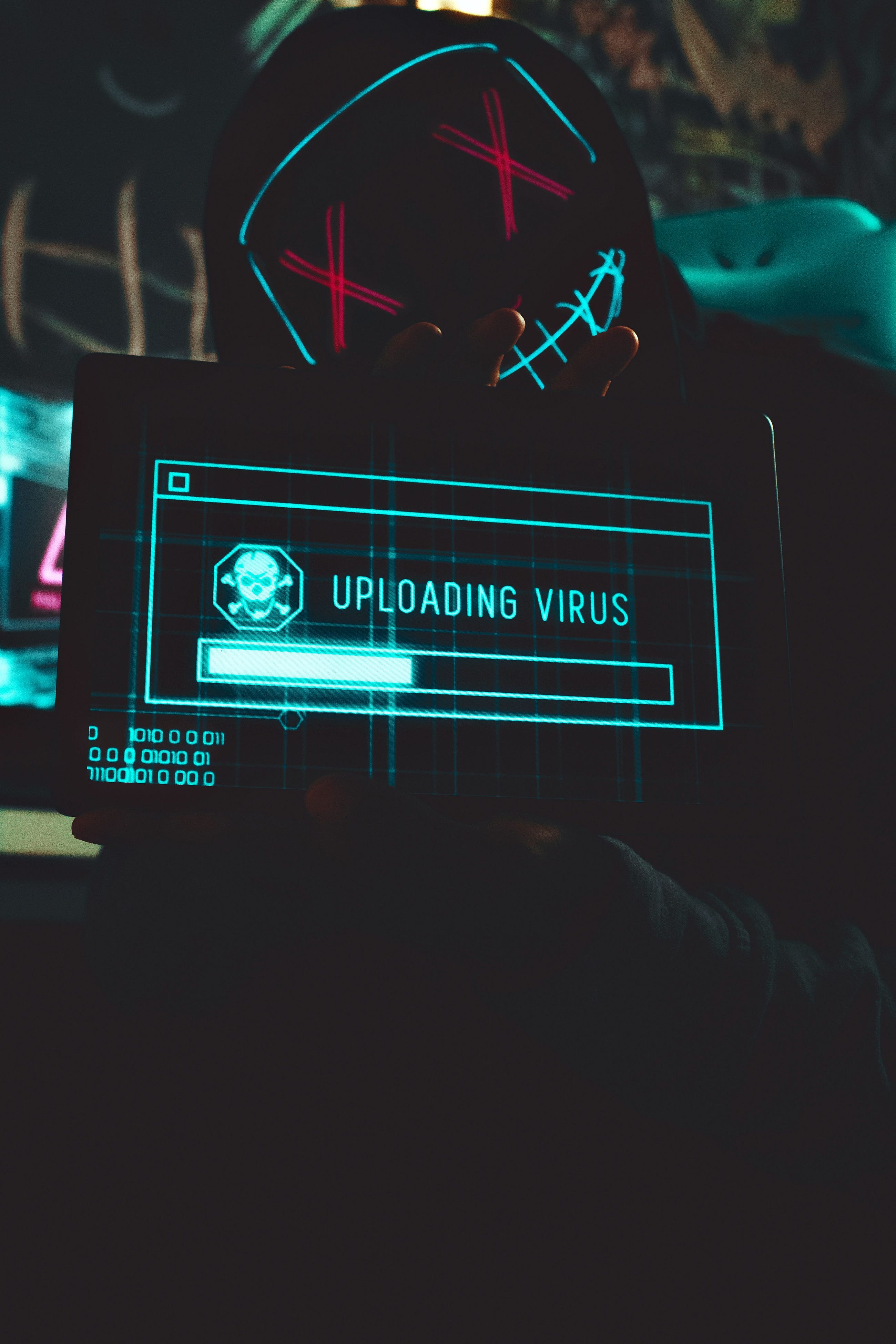 The image of a masked figure holding a screen that says “Uploading Virus” may look like something…
