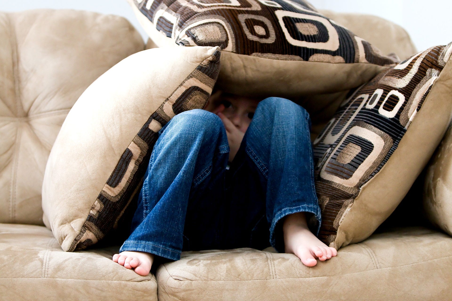 A child hiding behind sofa cushions