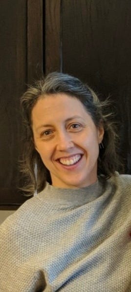Selfie of a white woman smiling at the camera. She is wearing a light sweater and has shoulder-length hair.