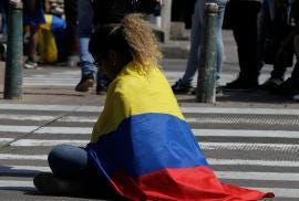 Picture of a young woman sitting on the street covered by colombian flag.
