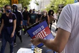 Person holding clipboard with text saying “Register to vote” in front of line of people