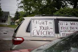 A silver van with a poster that says “Fight Your Eviction” taped on the backseat window