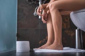 Picture of a person sitting on a toilet showing only legs from the knees. Tissue roll on the floor by their legs