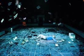 An image from a stage play of The Curious Incident of the Dog in the Night-Time. A white teenage boy lies on a stage divided into a grid.