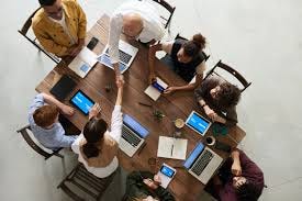 people sitting around a table with laptops — two are shaking hands