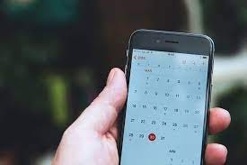 Hand holding a cell phone. Calendar on screen of phone.