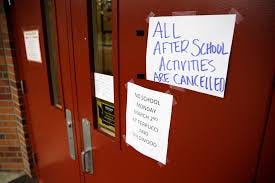 Red school door with handwritten sign taped saying “ALL AFTER SCHOOL ACTIVITIES ARE CANCELLED”