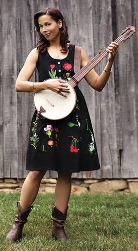 Rhiannon Giddens with a banjo in front of a barn.