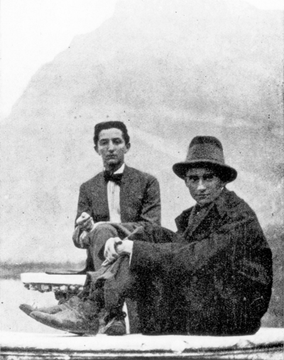 A imagem mostra Franz Kafka e seu amigo Max Brod sentados em um barco. Kafka está usando um chapéu. A foto está em preto e branco, apresentando um estilo retrô. Ambos os indivíduos estão formais.