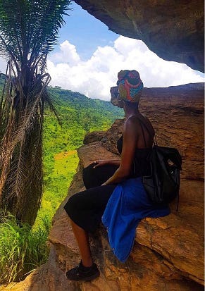 Woman in a headwrap sits sideways on brown rocks, looking into the green mountains.