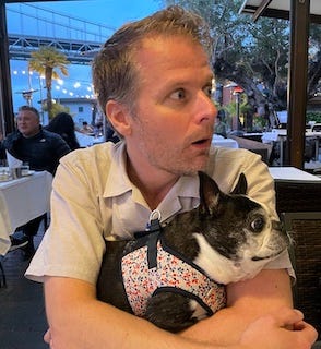 A picture of the author making a silly face with his dog while at dinner.