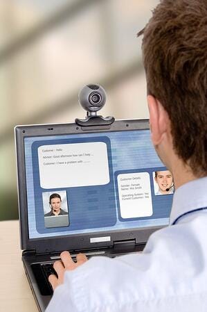 A man sitting at a laptop with a webcam on top, chatting with two people over video conference