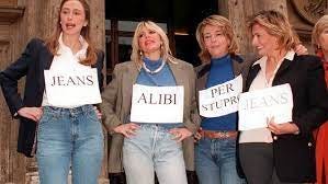 Four women from the Italian Parliament protesting by wearing jeans and carrying signs with roughly one word each saying “Jeans Alibi Per Stupro”. This saying translates to “Jeans: An Alibi for Rape