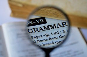 A grammar book being looked at through a magnifying glass so the word Grammar is large and the rest of the page is blurry.