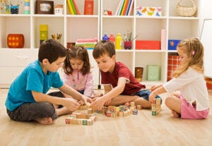 Children with autism playing with blocks in a room, promoting speech therapy progress.