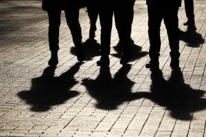 Crowd walking down on sidewalk, concept of strangers, crime, society, epidemic, population. Silhouettes and shadows of people on the street.