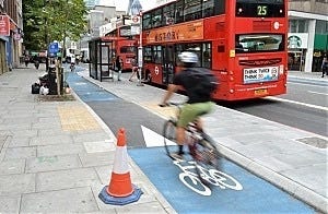 Photo of London floating bus stop with bicyclist in the lane that means they avoid parked buses but cut across pathway for pedestrians trying to get to bus stop