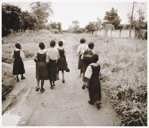 Ugandan school girls walk down a muddy dirt road in Gulu