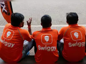 3 men sitting on a stairs facing back with logo on their tshirt naming “Swiggy”