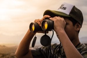Man with cap looking through binoculars