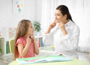 A woman in a white coat engages in conversation with a young girl, aiding in the progress of speech therapy for children with autism.