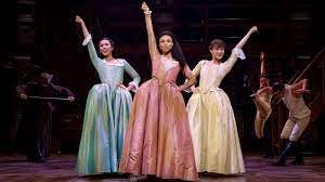 Three women (blue, pink and yellow dresses) click one hand high in the air with the other on their hip