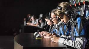 A bunch of teenagers at a table wearing blue and black team jerseys and white long sleeve shirts, wearing headphones and playing on a phone