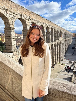 A woman in a long white coat stands on a bridge overlooking aquaducts.