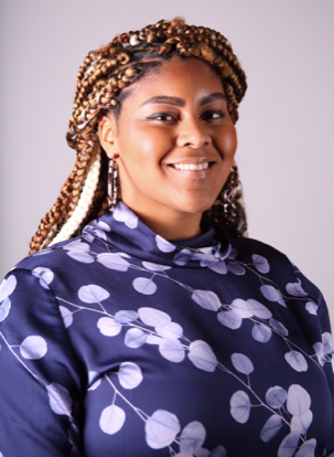 Dr. Keila Miles, smiles at the camera. She is wearing a purple floral blouse, her hair is styled in braids and pulled back.