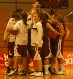 A group of women in a huddle on the basketball court, with their hands touching above their heads