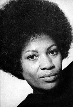 Black and white image from the 1970s featuring author Toni Morrison, sporting an afro hairstyle in a black turtleneck sweater. This image was from the dustjacket of one of her books.