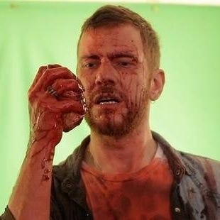 A photo of director Jason Lei Howden, covered in blood, holding a fake human heart in one palm.