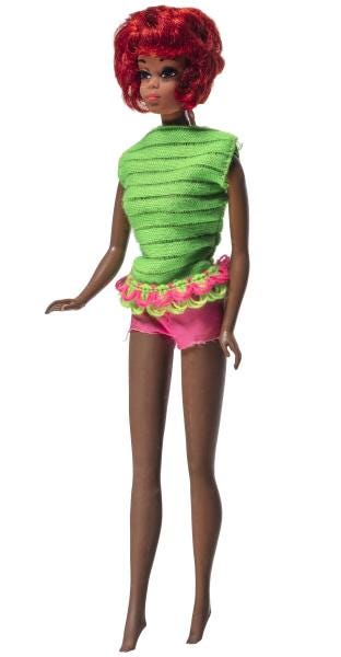 Image is of the Talking Christie Doll. She’s Black with dark skin and red hair cut in a curly bob. She’s wearing a green top and pink shorts.