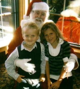 A 6 year old and an 8 year old on Santa’s lap. All are smiling.