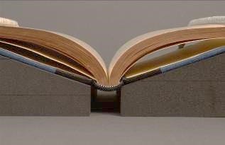 A tightback half leather bound book, resting open on 2 foam book supports, with space left between them for the rounded spine