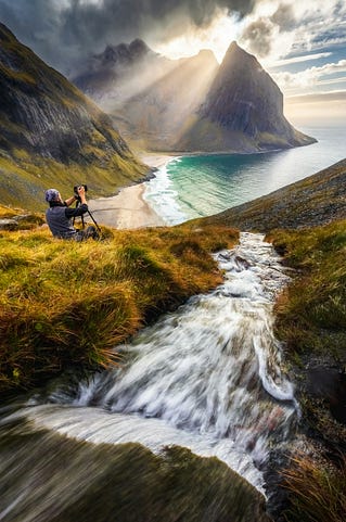 a river flows down a mountain to the sea where a photographer sits