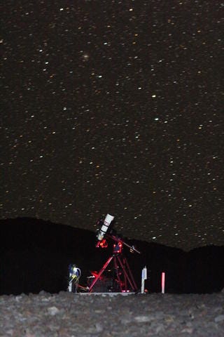 A white telescope on a red support stands before a starry night sky.