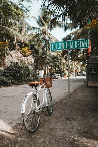 A bicycle on a pretty street next to a sign that says “Follow that Dream”