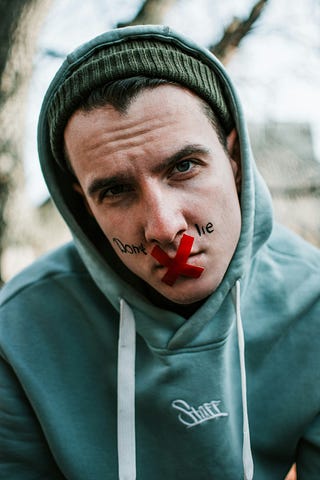 A man with red tape across his lips and the mention ‘Don’t lie’ written across his face.