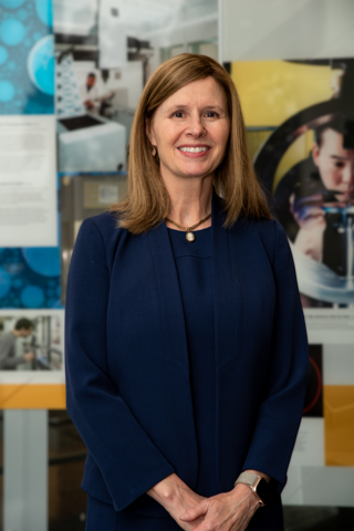 Laurie Locascio poses for a photo in front of a collage of NIST images.