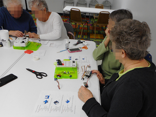 Four older adults split into pairs, seated at a table working on an activity with a Grove Arduino toolkit.