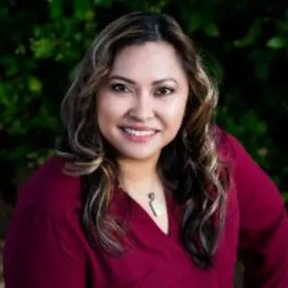 Photo of Dr. Tracy Ocampo in a red sweater with plants in the background.