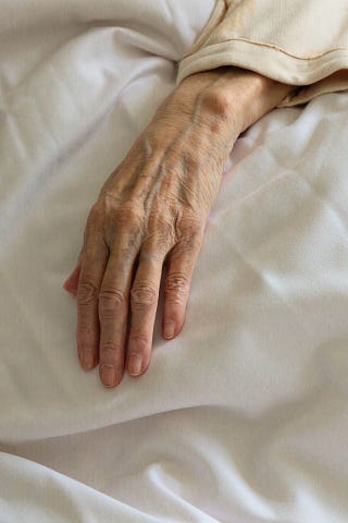 An elderly woman with beautiful hands on a white blanket