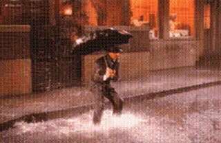 Gif de cena de chiva, com homem vestido de paletó e chapéu, pulando em uma grande poça d'água no paralelepípedo da rua, segurando um guarda-chuva.
