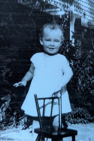 A young infant grandmother in a black and white photograph holding onto a chair.