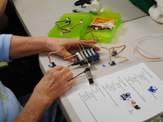 An older adult’s hands working with a Grove Arduino Toolkit with wires coming out of the shield to connect to components.