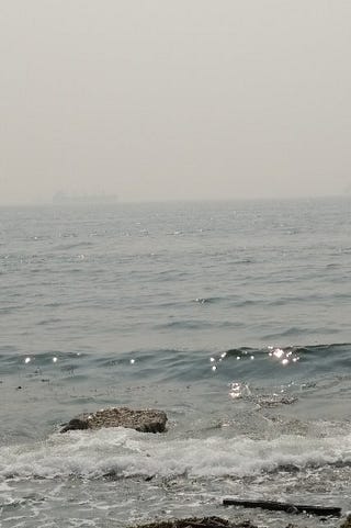 A picture of the thick smokey haze over water with a distant ship almost obliterated by smoke.