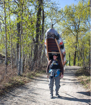 Male canoeist walking to the river carrying boat on his head.